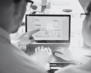 Une photo en noir et blanc avec deux personnes de dos qui montrent un écran avec une facture électronique dessus.