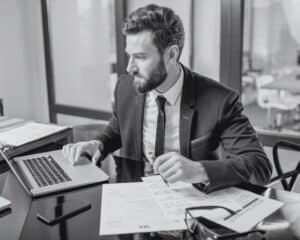 Visuel d'illustration sur le pilotage de ses données financières avec Cashlab. Un homme utilise un ordinateur avec des documents sur le côté contenant ses données financières.